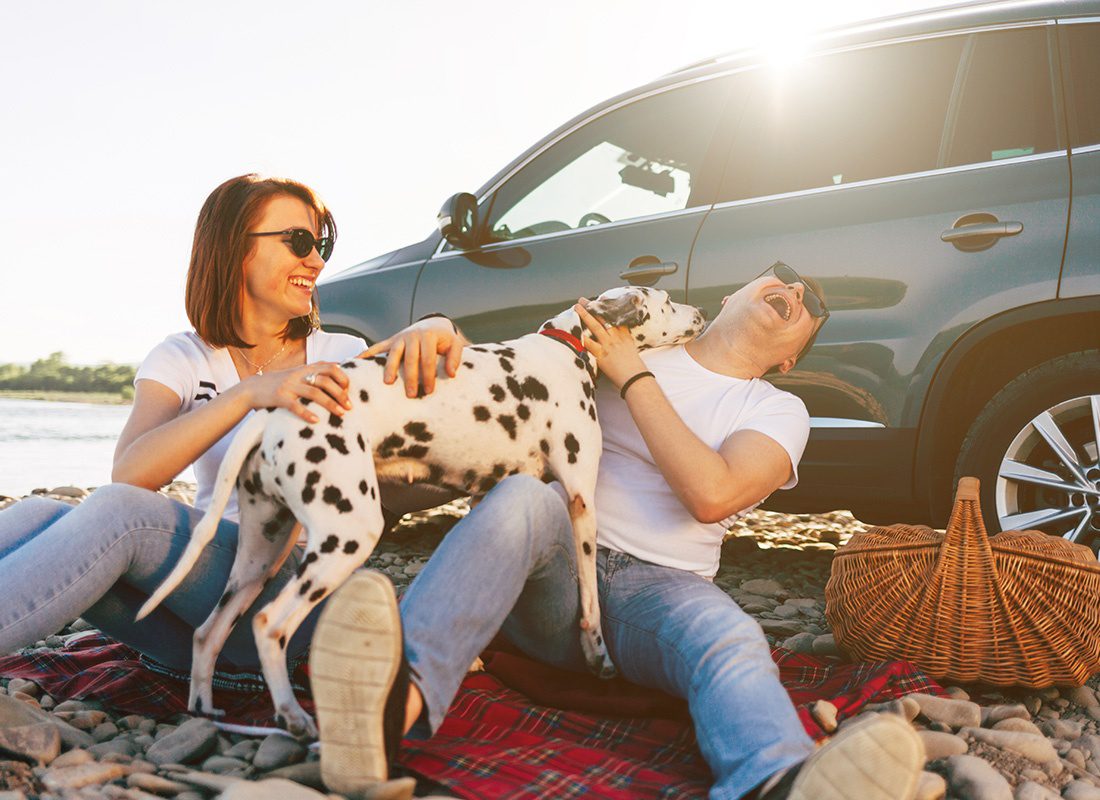 Insurance Solutions - Portrait of a Young Couple Having Fun Playing with Their Dog by the Lake on a Summer Road Trip