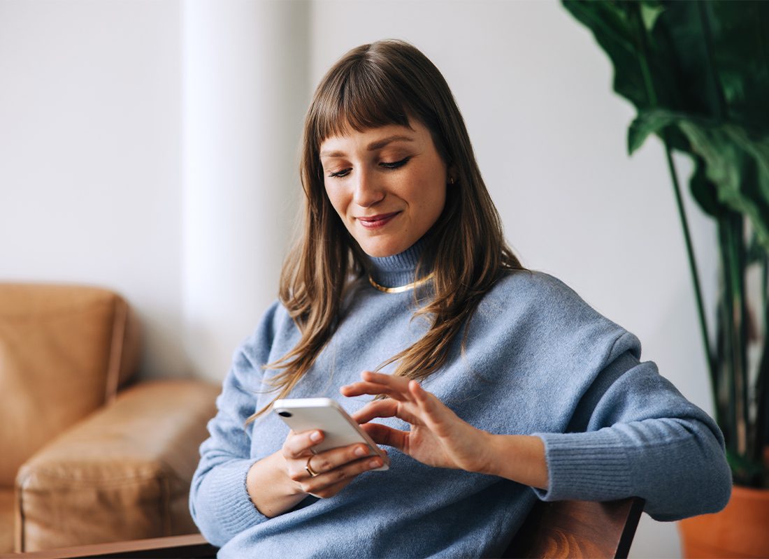 Text Opt-In - Woman Looking Down at Her Phone While Sitting on the Couch at Home